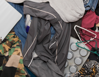 Cluttered pile of assorted items including clothing, hangers, a camouflage-patterned garment, a muffin tray, and a white binder, all arranged in a disorganized manner.