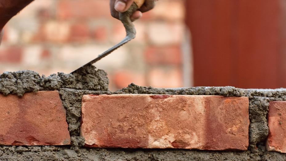A close-up of a hand using a trowel to apply mortar between red bricks while constructing a brick wall. A close-up of a hand using a trowel to apply mortar between red bricks while constructing a brick wall.