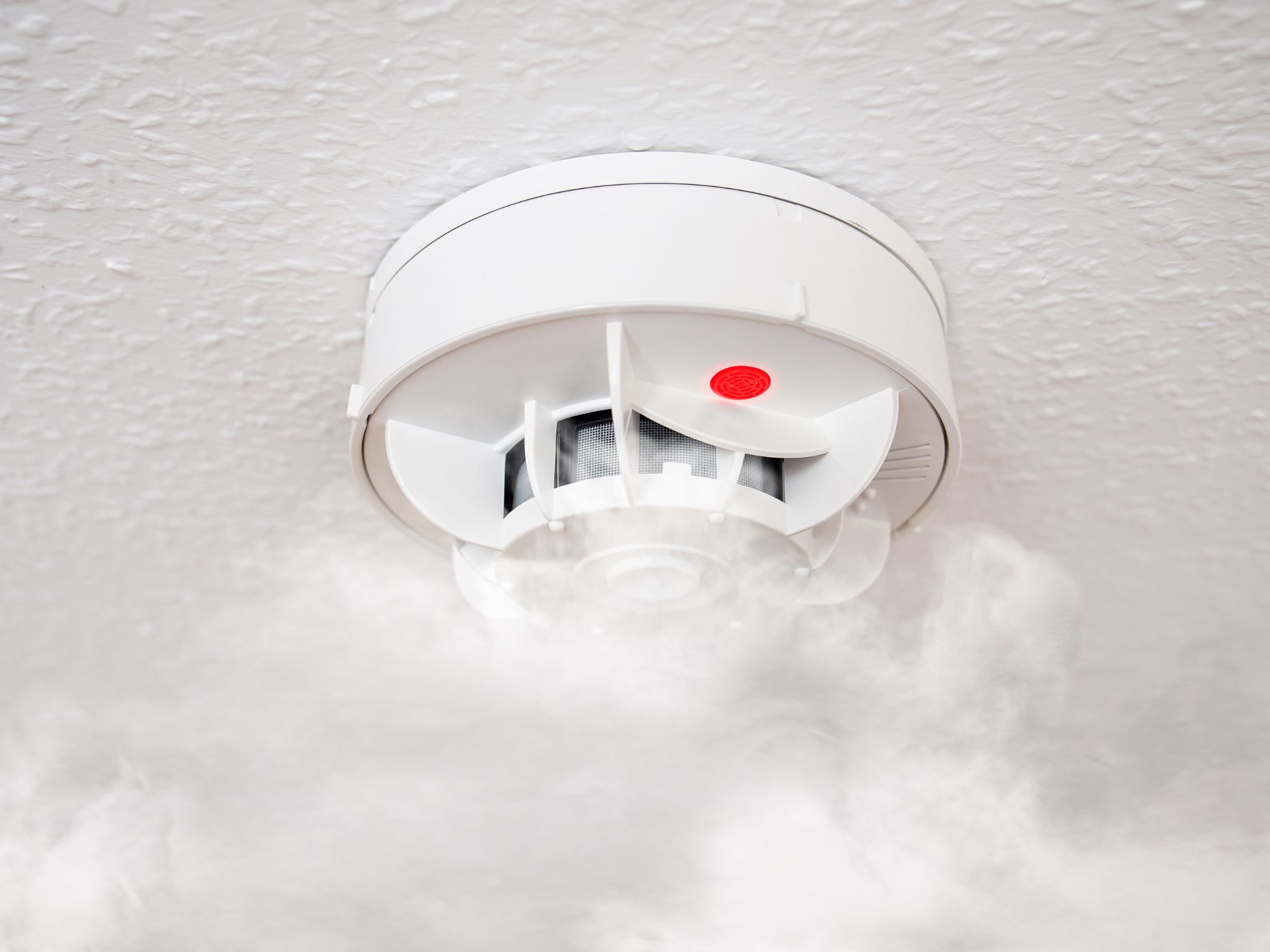Smoke detector with red light activated and smoke rising around it.