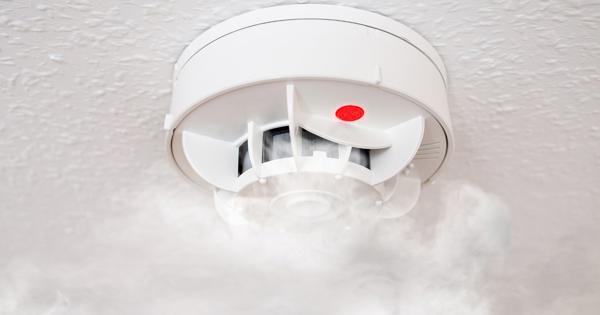 Smoke detector with red light activated and smoke rising around it.
