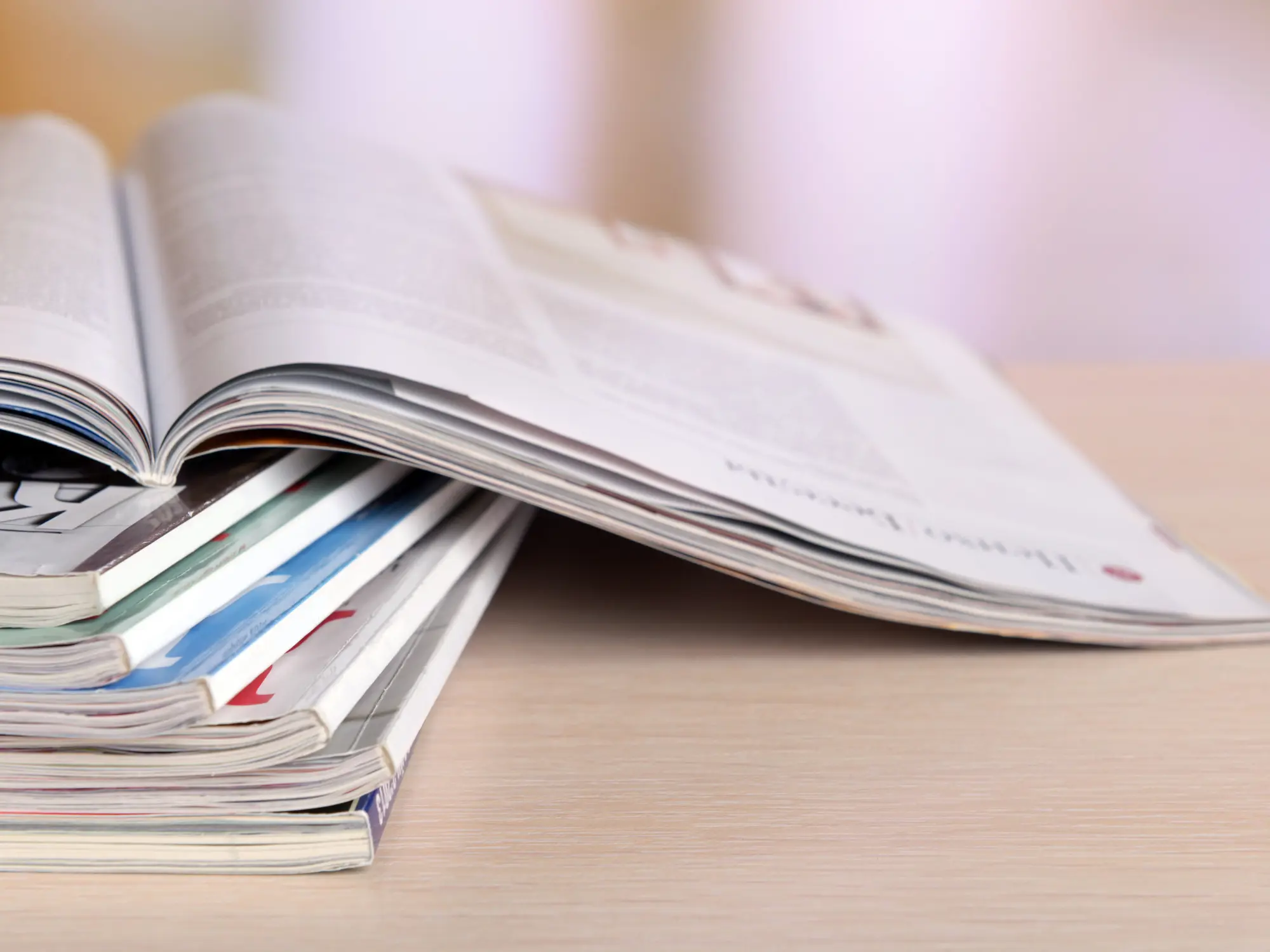 A stack of magazines with one open on top, displaying printed text and images, representing reading materials or publications.