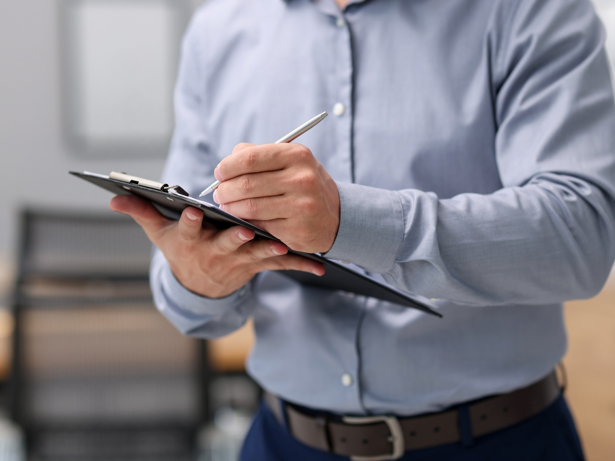 Close-up of a person writing notes on a clipboard during an indoor inspection.