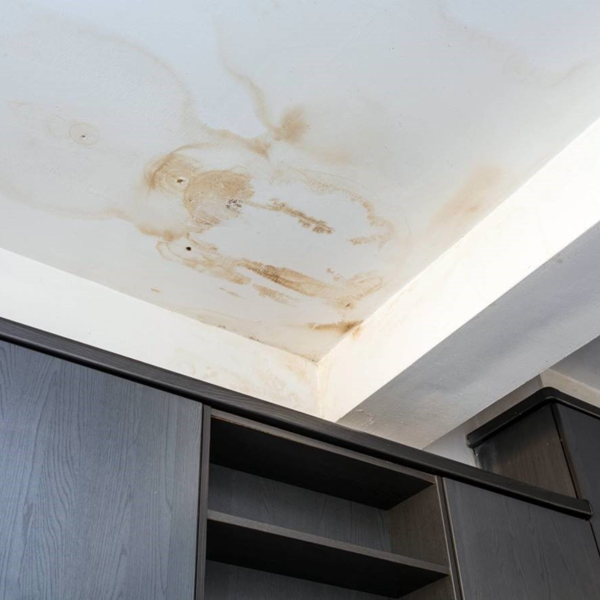 Ceiling corner with extensive brown water stains and damage above dark cabinets, likely caused by a roof or plumbing leak