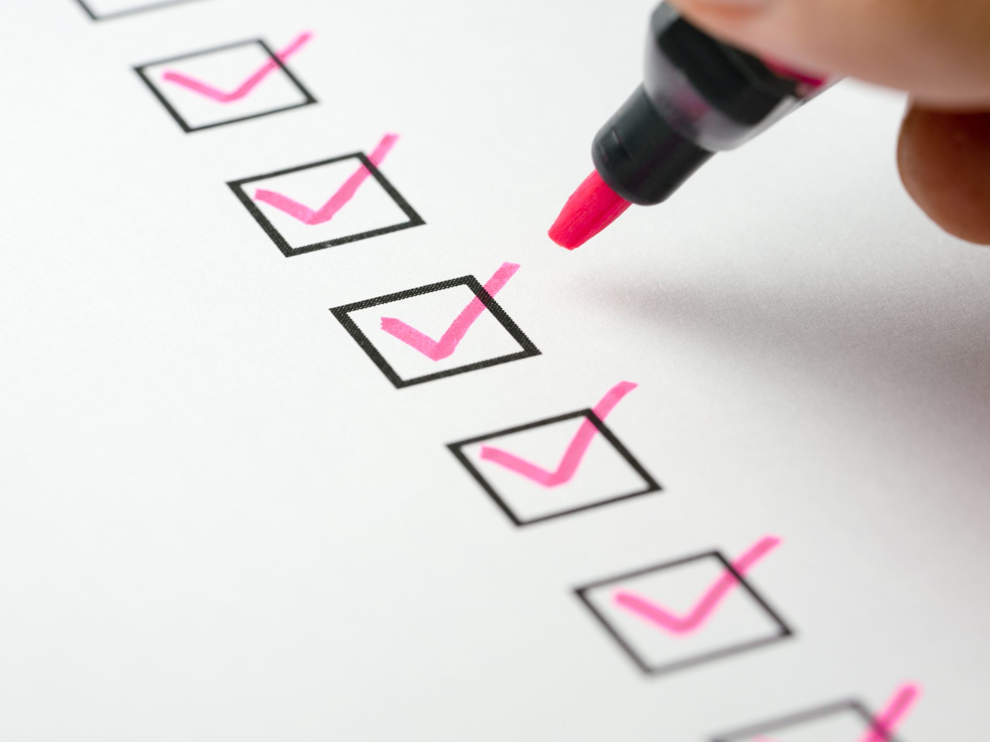 Hand holding a pink marker checking off items on a checklist, with three boxes already ticked.