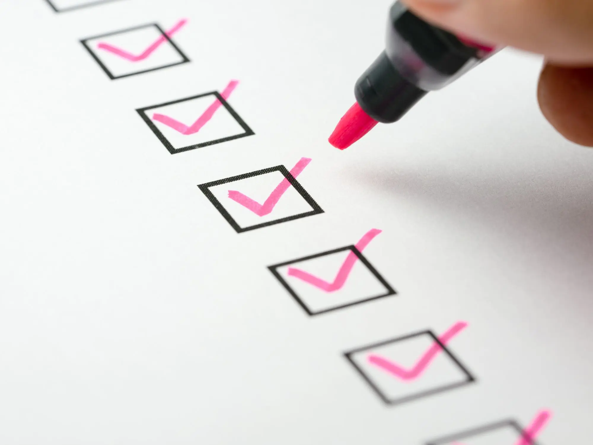 Hand holding a pink marker checking off items on a checklist, with three boxes already ticked.