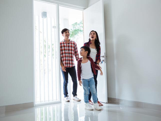 Family entering a bright, empty home through an open front door, stepping onto a polished floor. Family entering a bright, empty home through an open front door, stepping onto a polished floor.