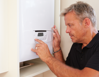 A technician adjusts the controls on a wall‑mounted boiler, pressing buttons on the digital control panel inside a cupboard.
