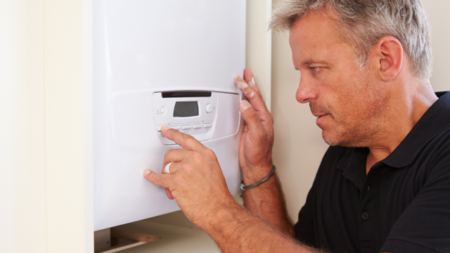 A technician adjusts the controls on a wall‑mounted boiler, pressing buttons on the digital control panel inside a cupboard.