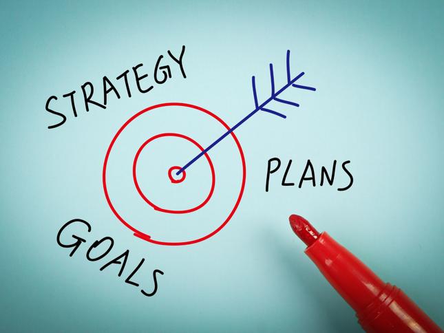 A red marker draws a target with an arrow hitting the bullseye, surrounded by the words "STRATEGY," "GOALS," and "PLANS," symbolizing the alignment of planning and strategy to achieve objectives. A red marker draws a target with an arrow hitting the bullseye, surrounded by the words "STRATEGY," "GOALS," and "PLANS," symbolizing the alignment of planning and strategy to achieve objectives.