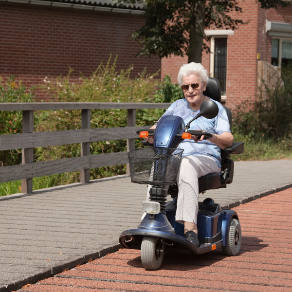 An individual riding a blue mobility scooter on a pathway outside a brick apartment building.