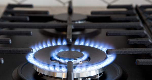 Close-up of a lit gas stove burner with blue flames, black metal grate, and white hexagonal tile background.