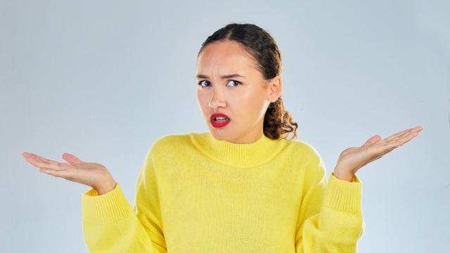 Person in a yellow sweater with raised hands against a grey background.