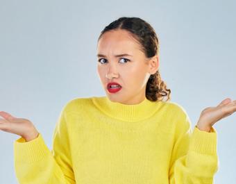 Person in a yellow sweater with raised hands against a grey background.