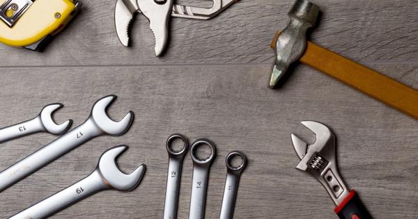 A variety of hand tools arranged on a wooden surface, including a yellow tape measure, two adjustable wrenches with orange and red handles, a yellow-handled hammer, and several open-end and combination wrenches labeled with sizes ranging from 10 to 17.