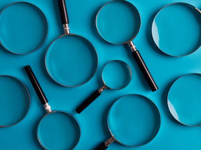 Several magnifying glasses of different sizes with black handles and silver rims arranged on a bright blue background. Several magnifying glasses of different sizes with black handles and silver rims arranged on a bright blue background.