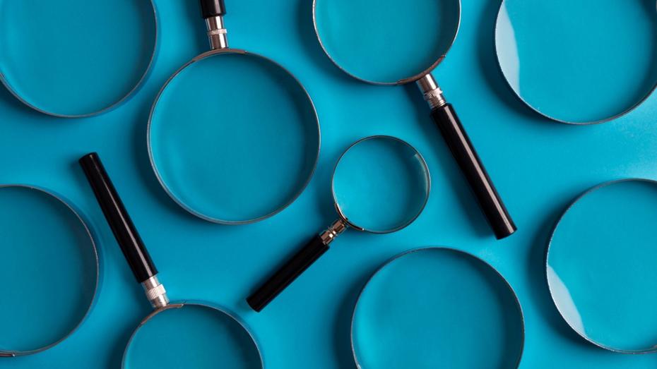 Several magnifying glasses of different sizes with black handles and silver rims arranged on a bright blue background. Several magnifying glasses of different sizes with black handles and silver rims arranged on a bright blue background.