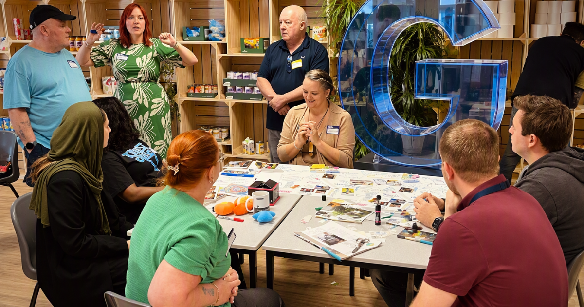 Residents and colleagues gathered around tables during a workshop or discussion session, with a large transparent blue letter G displayed in the room.