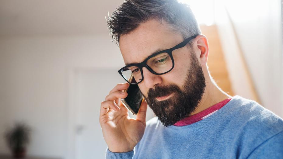 A person wearing glasses talking on the phone indoors. A person wearing glasses talking on the phone indoors.