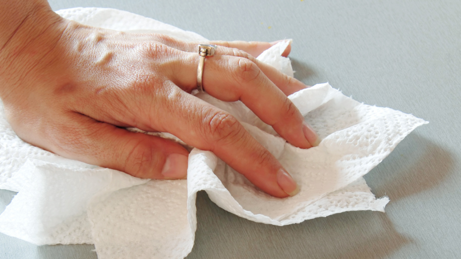 A hand using paper towels to wipe a surface clean. A hand using paper towels to wipe a surface clean.