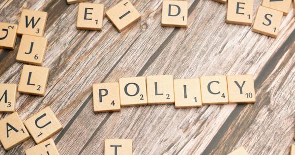 Scrabble tiles on a wooden surface spell out the word "POLICY" in the centre, with other random tiles scattered around.
