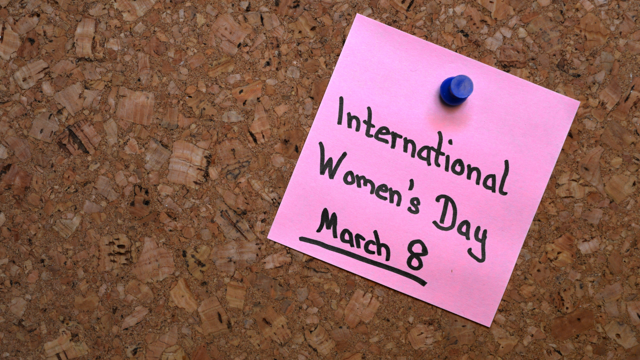“Pink sticky note pinned to a corkboard with a blue pushpin, handwritten with the words ‘International Women’s Day, March 8’.”