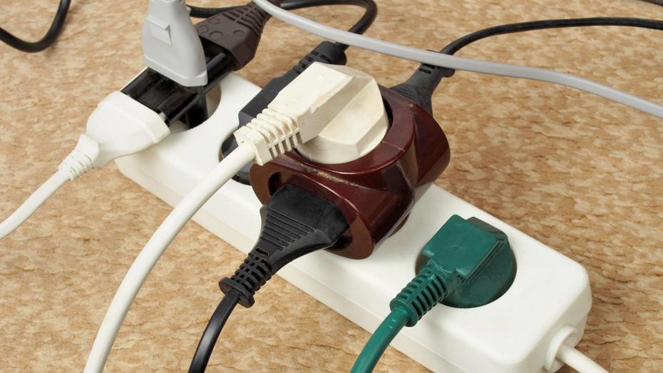 White power strip with six occupied outlets, featuring various colored plugs and adapters, placed on a beige carpeted floor. White power strip with six occupied outlets, featuring various colored plugs and adapters, placed on a beige carpeted floor.