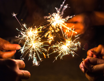 Close-up of several hands holding lit sparklers against a dark background.