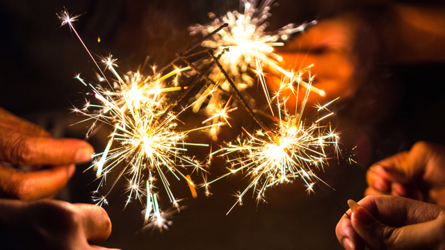 Close-up of several hands holding lit sparklers against a dark background.