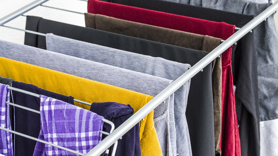 A drying rack filled with colorful clothes including yellow, gray, black, red, and purple plaid garments.  A drying rack filled with colorful clothes including yellow, gray, black, red, and purple plaid garments.