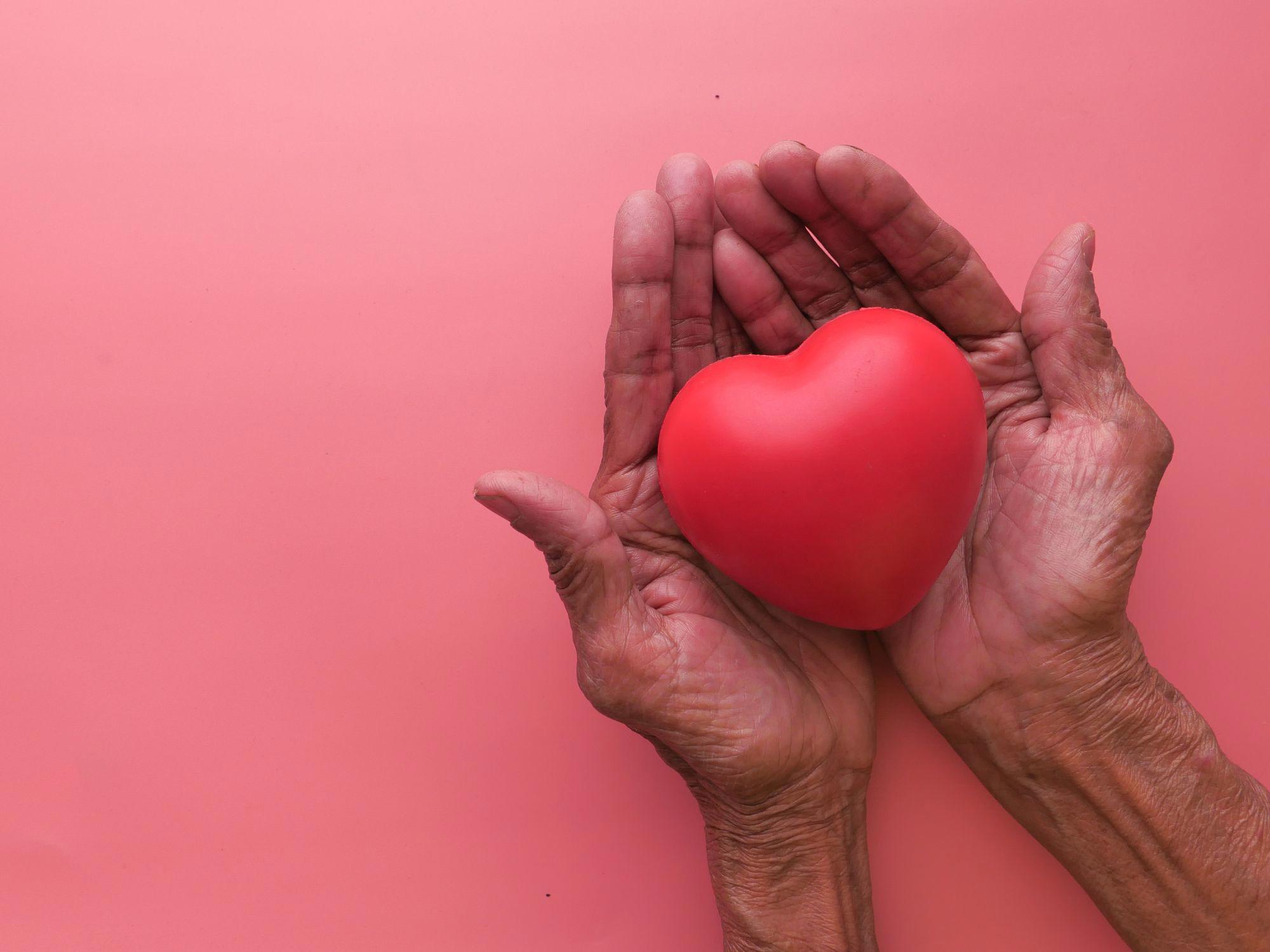 Two hands gently holding a red heart against a soft pink background, symbolising kindness, compassion, and support for a zero-tolerance approach to staff abuse.