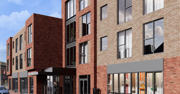 A modern brick building showing large windows, shopfronts and bicycle stands on the pavement. A person walks toward the entrance beneath a canopy.