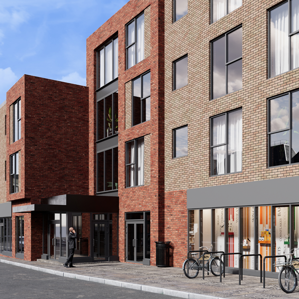 A modern brick building showing large windows, shopfronts and bicycle stands on the pavement. A person walks toward the entrance beneath a canopy.