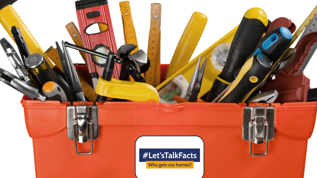 Red metal toolbox filled with assorted hand tools including screwdrivers, rulers, pliers and a spirit level, with a speech-bubble sticker on the front reading “#Let’sTalkFacts – Who gets our homes?”.