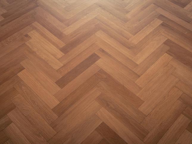 Wooden floor with a herringbone pattern made of rectangular planks in varying shades of brown. Wooden floor with a herringbone pattern made of rectangular planks in varying shades of brown.