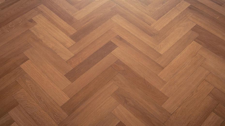 Wooden floor with a herringbone pattern made of rectangular planks in varying shades of brown. Wooden floor with a herringbone pattern made of rectangular planks in varying shades of brown.