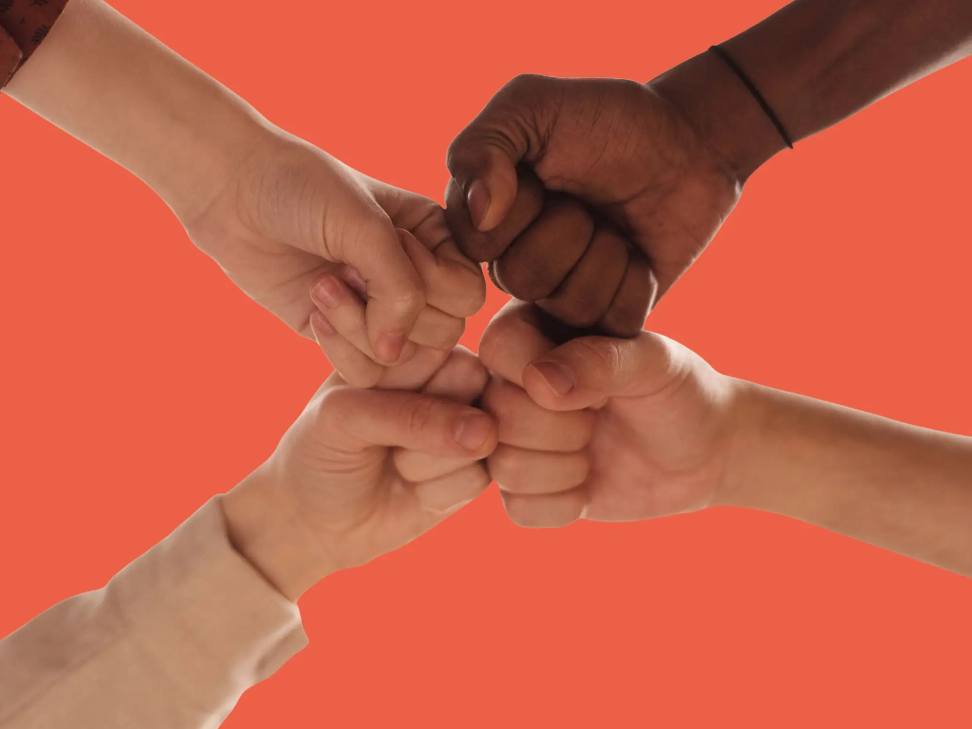 Four hands coming together in a fist bump against an orange background, symbolising unity and teamwork.