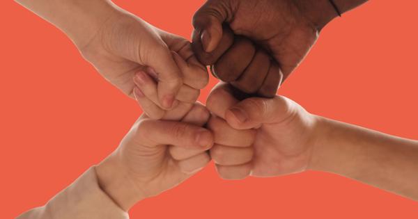 Four hands coming together in a fist bump against an orange background, symbolising unity and teamwork.