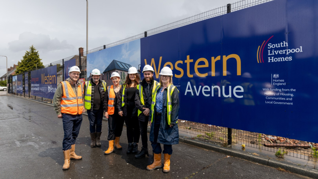 Group of six people in construction gear standing beside a large blue sign that reads 'Western Avenue' with logos for South Liverpool Homes and Homes England, and funding acknowledgment from the Ministry of Housing, Communities and Local Government.