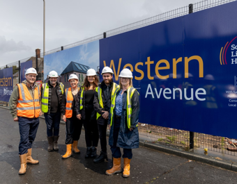 Group of six people in construction gear standing beside a large blue sign that reads 'Western Avenue' with logos for South Liverpool Homes and Homes England, and funding acknowledgment from the Ministry of Housing, Communities and Local Government.