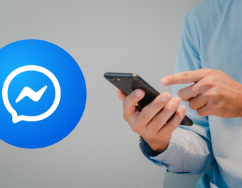 Person in a light blue shirt using a smartphone next to a large Facebook Messenger logo.