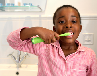 A child brushing their teeth with a green toothbrush in a bathroom.