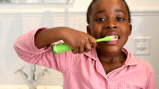 A child brushing their teeth with a green toothbrush in a bathroom.