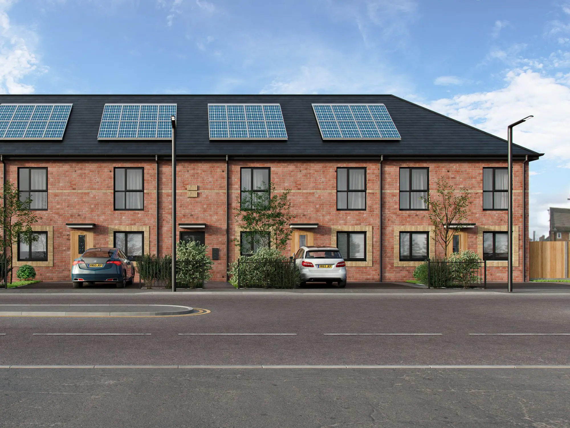 A two-storey apartment block with black roof and rooftop solar panels. A blue and a white car are parked in front, with streetlights lining the empty road under a partly cloudy sky.