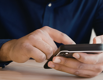 A person wearing a dark long‑sleeved shirt uses a smartphone, holding it in one hand and tapping the screen with the other.