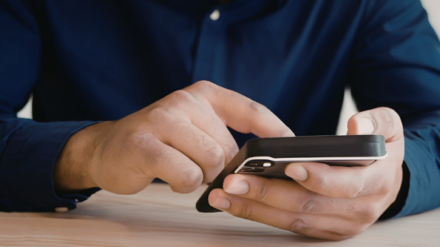 A person wearing a dark long‑sleeved shirt uses a smartphone, holding it in one hand and tapping the screen with the other.