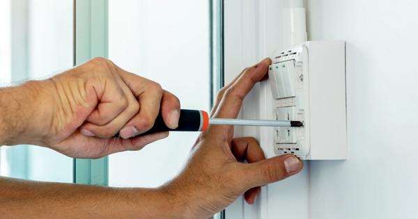 Close-up of hands using a screwdriver to install or repair an electrical wall switch next to a glass door or window.
