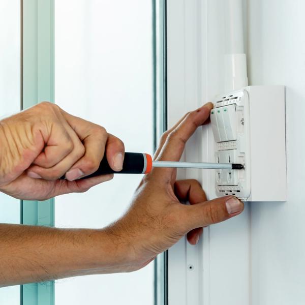 Close-up of hands using a screwdriver to install or repair an electrical wall switch next to a glass door or window.