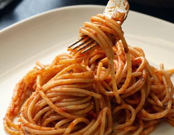 A white plate of spaghetti topped with tomato sauce, with a fork lifting a twirl of pasta to showcase its texture and coating