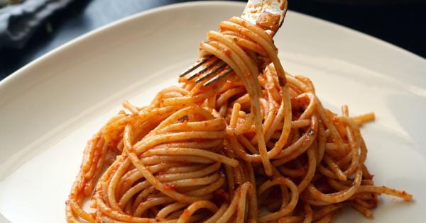 A white plate of spaghetti topped with tomato sauce, with a fork lifting a twirl of pasta to showcase its texture and coating