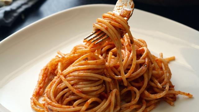 A white plate of spaghetti topped with tomato sauce, with a fork lifting a twirl of pasta to showcase its texture and coating